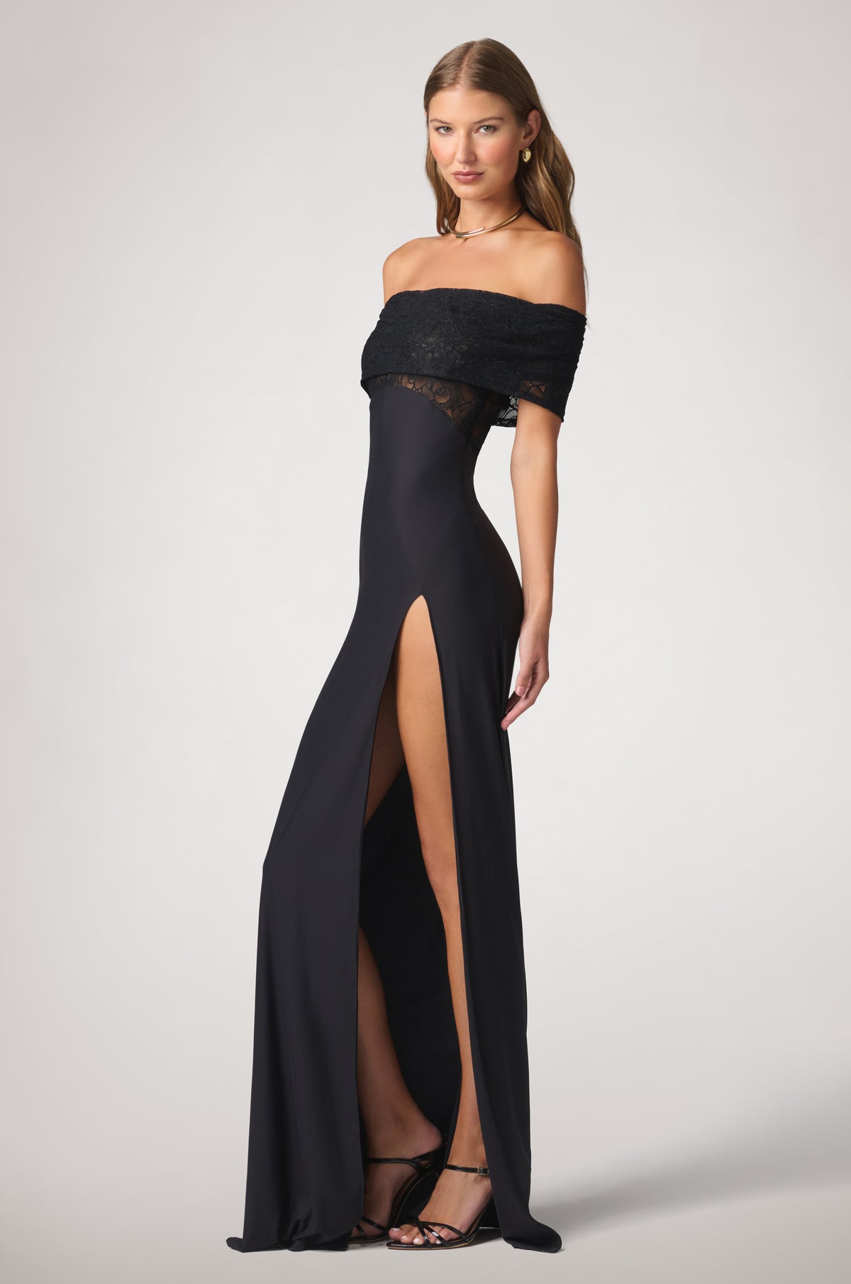 Figure-skimming profile with softly draped lace at the shoulders and a defined waist, opening into a long, fluid skirt with a dramatic side slit.

